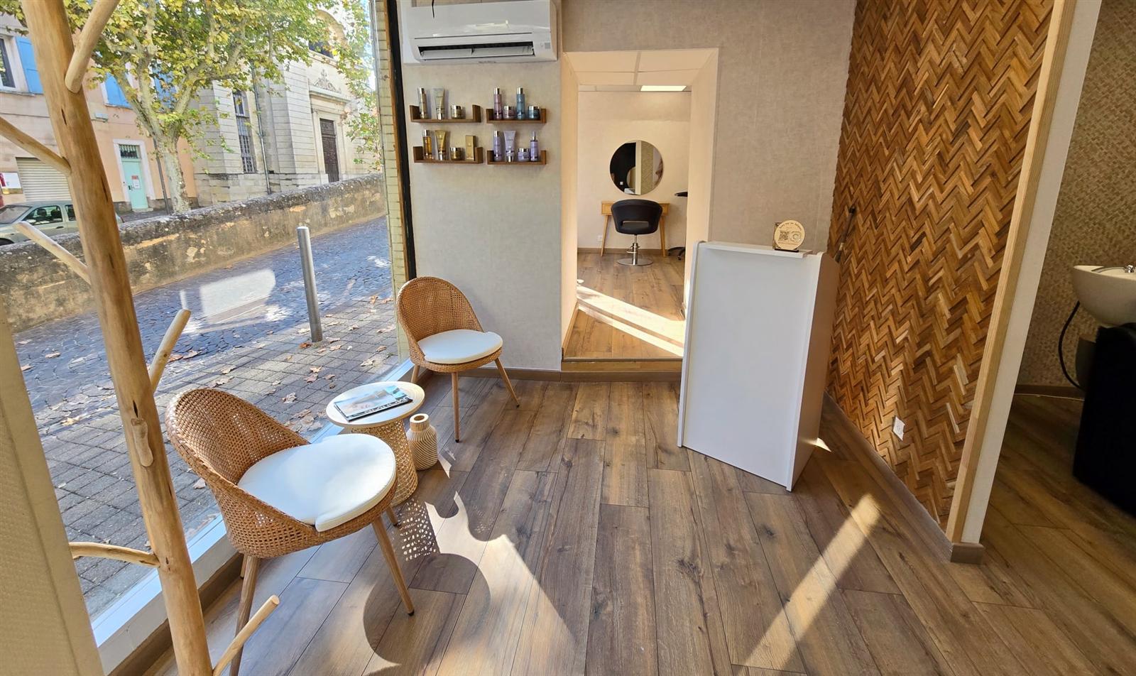 L’entrée du salon Hair Place : fauteuils en rotin devant la vitrine, mur en bois en point de Hongrie et étagères de produits Wella