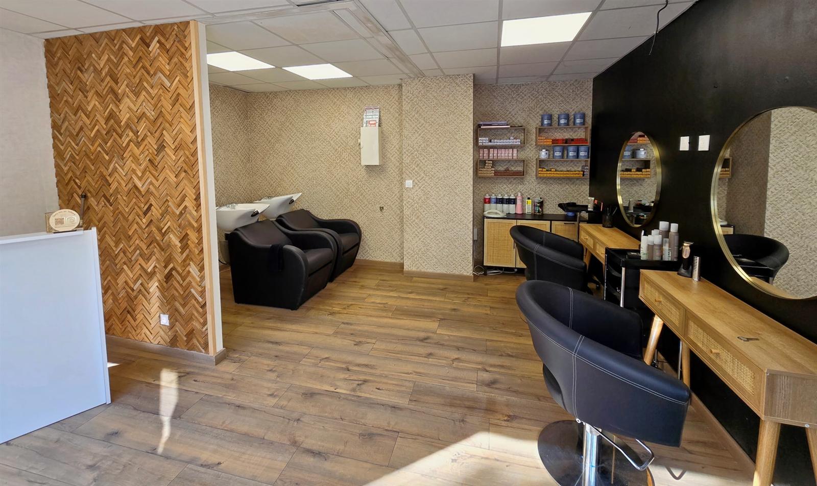 Le plateau de coiffure : fauteuils noirs, consoles en bois et rotin, grands miroirs ronds dorés et bacs à shampoing